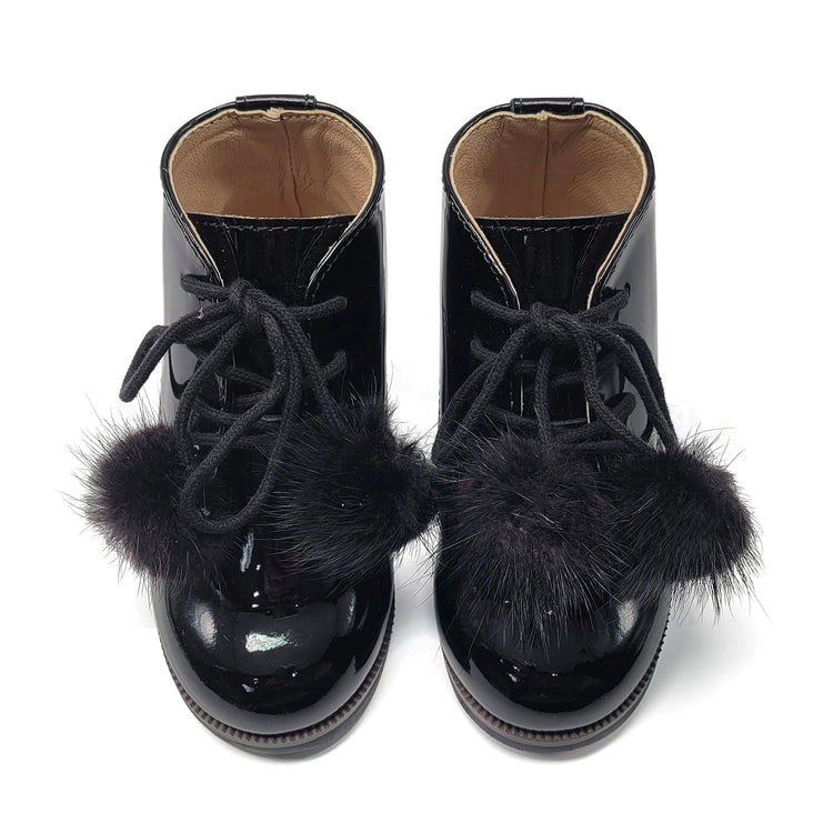 Black patent leather boots with fur pom-poms on a white background