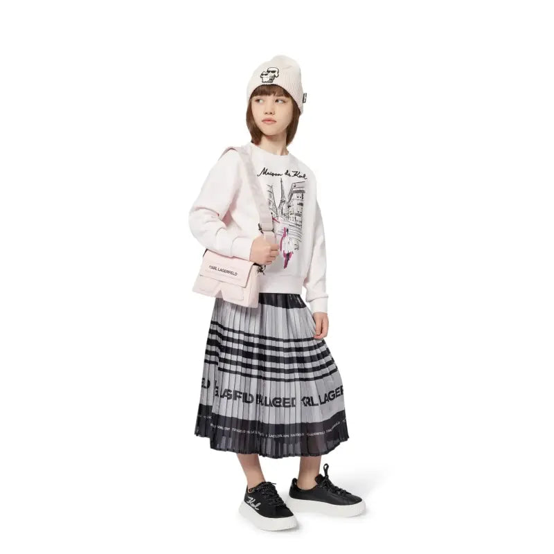 Child wearing a white sweater with graphic design, plaid skirt, and black shoes on a white background