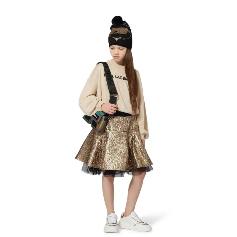 Person wearing a beige sweater, gold sequin skirt, and black beanie with sunglasses on a white background