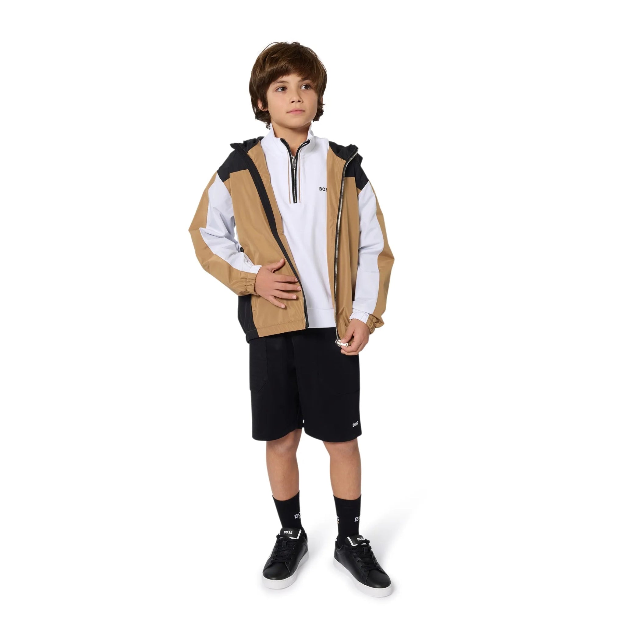 Child wearing a beige and black jacket with a white shirt, black shorts, and black shoes on a white background.