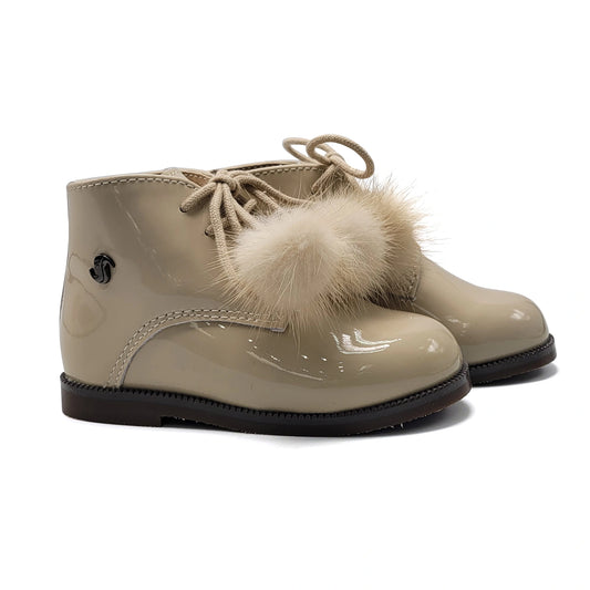 Beige patent leather boots with fur pom-poms on a white background