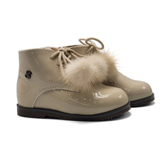 Beige patent leather boots with fur pom-poms on a white background
