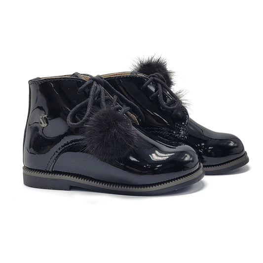 Black patent leather boots with fur pom-poms on a white background