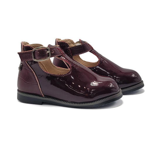 Pair of shiny maroon shoes with buckles on a white background
