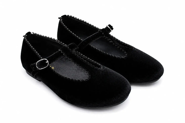 A pair of black velvet Mary Jane flats with braided trim and small silver buckle details, shown on a white background.