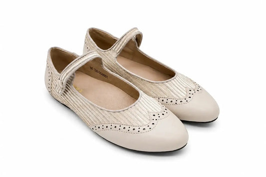 A pair of kids Mary Jane flats in a light beige color, featuring a textured woven upper, perforated brogue detailing on the toe, and a single hook-and-loop strap closure, shown against a plain white background.