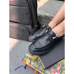 Person wearing black textured shoes with a black bag and book on a concrete surface